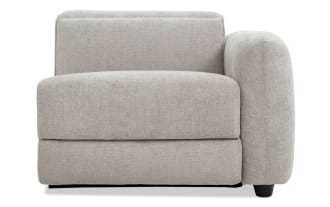 Modern beige fabric sectional sofa corner chair with plush cushions and rounded armrest, featuring textured upholstery and dark wooden legs.