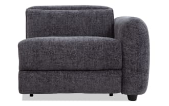 Dark gray upholstered modern corner sofa chair with plush cushioning, rounded armrest, and short black legs, suitable for living room seating.
