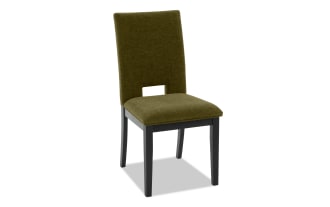 Upholstered dining chair with olive green fabric seat and backrest, black wooden legs, and a rectangular cutout detail on the back.
