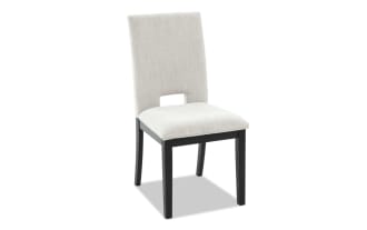 Upholstered dining chair with beige fabric seat and backrest, black wooden legs, and a rectangular cutout at the lower back.