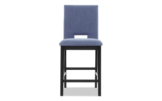 Upholstered bar stool with blue fabric seat and backrest, black wooden legs, and a rectangular cutout in the backrest for modern dining or kitchen use.