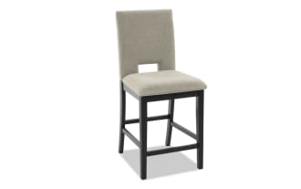 Upholstered beige fabric counter-height chair with black wooden legs, rectangular cutout backrest, and padded seat for dining or kitchen use.