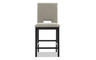 Upholstered beige fabric counter-height chair with black wooden legs, rectangular cutout backrest, and padded seat for dining or kitchen use.