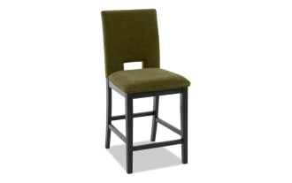 Upholstered bar stool with olive green fabric seat and backrest, black wooden legs, and footrest, modern dining seating.