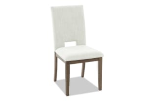Upholstered dining chair with light beige fabric, wooden legs in dark brown finish, and a rectangular cutout in the backrest for modern style.