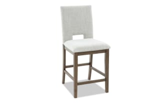 Upholstered bar stool with light gray fabric seat and backrest, wooden legs with footrest, modern dining or kitchen seating.
