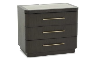 Dark wood three-drawer nightstand with rounded edges and long horizontal brass handles, modern bedroom furniture design.