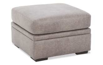 Gray leather ottoman with cushioned top and dark wooden legs, featuring a soft textured finish and modern rectangular design.