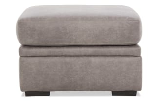 Gray leather ottoman with cushioned top and dark wooden legs, featuring a soft textured finish and modern rectangular design.