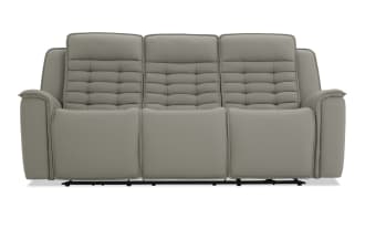Gray leather reclining three-seater sofa with padded backrests and armrests, featuring horizontal stitching and cushioned footrests for comfort.