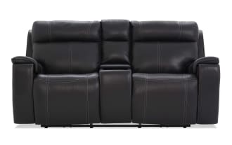 Black leather reclining loveseat with contrast stitching, padded armrests, and a center console for storage or cup holders, ideal for home theater seating.