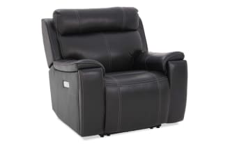 Black leather recliner chair with padded armrests, cushioned backrest, and visible white stitching, designed for comfort and modern living rooms.