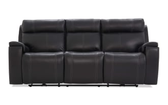 Black leather reclining sofa with three seats, featuring plush cushioning, visible white stitching, and padded armrests for living room comfort.