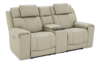 Beige leather reclining loveseat with padded armrests, adjustable headrests, and a central console for storage or cup holders, designed for comfort and style.