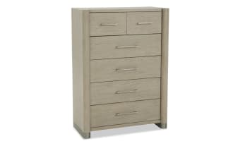 Tall light oak wood dresser with five drawers, featuring modern metal handles and rounded vertical side panels, ideal for bedroom storage.