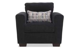 Dark gray upholstered armchair with wide padded arms, cushioned back, and a rectangular patterned lumbar pillow, featuring wooden block legs.