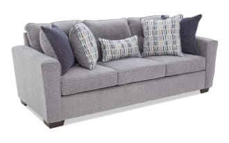 Modern gray fabric sofa with three seat cushions, dark wooden legs, and six decorative pillows in blue and patterned designs, ideal for living room seating.
