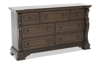 Traditional wooden dresser with dark brown finish, ornate carved details, and nine drawers featuring decorative metal handles, ideal for bedroom storage.