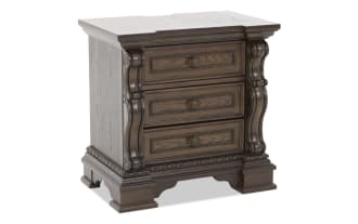 Dark brown wooden nightstand with three ornately carved drawers, decorative molding, and a classic vintage design.