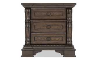 Dark brown wooden nightstand with three ornately carved drawers, decorative molding, and a classic vintage design.