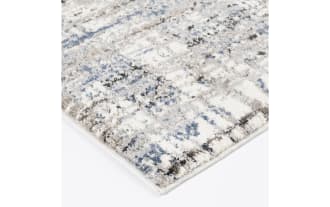 Area rug with an abstract pattern in shades of beige, blue, and gray on a white background, featuring a textured, modern design.
