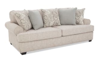 Beige fabric sofa with rolled arms, two large seat cushions, and five decorative throw pillows in paisley and solid patterns, modern style.