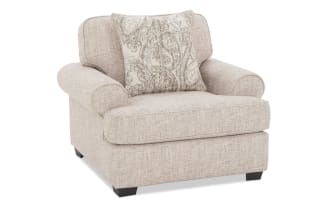 Beige fabric armchair with rounded arms and dark wooden legs, featuring a decorative beige and gray patterned throw pillow.