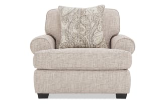 Beige fabric armchair with rounded arms and dark wooden legs, featuring a decorative beige and gray patterned throw pillow.
