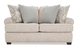 Beige fabric loveseat with rolled arms, featuring two solid light gray and two patterned beige-blue throw pillows, ideal for cozy living rooms.