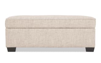 Beige fabric upholstered rectangular storage ottoman with cushioned top and dark wooden legs, suitable for living room seating and storage.