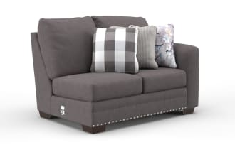 Gray fabric loveseat with three decorative pillows featuring checkered, houndstooth, and abstract patterns, accented with silver nailhead trim.