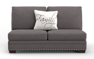 Gray fabric loveseat sofa with dark wooden legs and silver nailhead trim, featuring a white decorative pillow with the text "Family is forever" in elegant script.