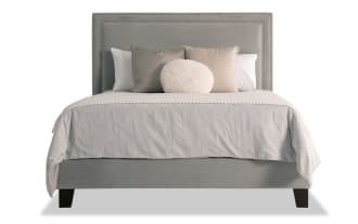 Tremont King Gray Upholstered Panel Bed with gray polyester fabric, rubberwood frame, and nailhead trim, featuring a transitional style and decorative pillows.