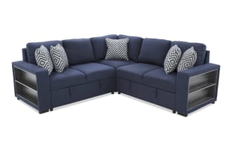 Blue fabric sectional sofa with built-in gray wood storage shelves on the armrest, featuring patterned throw pillows and modern design.
