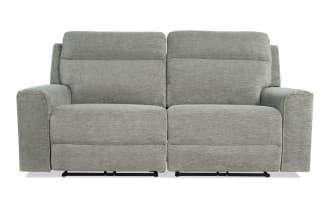 Modern gray fabric reclining loveseat with plush cushioning, wide armrests, and a contemporary design ideal for living room comfort.