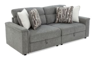 Gray fabric reclining sofa with soft cushions, featuring two patterned and two plain white throw pillows, modern design with padded armrests.