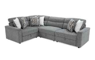 Gray fabric sectional sofa with L-shape design, tufted back cushions, and assorted decorative pillows in white and patterned brown tones.
