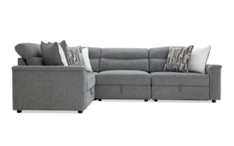 Gray fabric sectional sofa with L-shape design, tufted back cushions, and assorted decorative pillows in white and patterned brown tones.