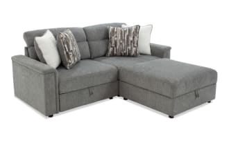 Gray fabric sectional sofa with chaise lounge, featuring tufted back cushions and four decorative pillows in neutral tones, modern design.