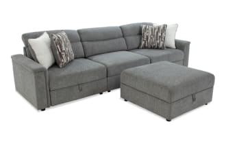 Gray fabric sectional sofa with a matching ottoman, featuring plush cushions, two patterned and two solid accent pillows, and a modern design.
