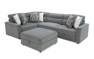 Gray fabric sectional sofa with matching ottoman, featuring plush cushions, patterned and solid throw pillows, and a modern design.