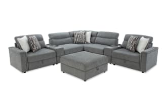 Gray fabric sectional sofa with adjustable headrests, plush cushions, patterned and solid throw pillows, and a matching ottoman for living room seating.