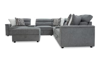 Gray fabric sectional sofa with adjustable headrests, plush cushions, patterned and solid throw pillows, and a matching ottoman for living room seating.