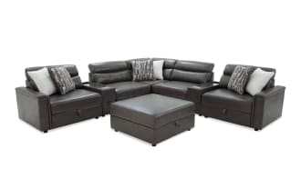 Dark gray leather sectional sofa with ottoman, featuring cushioned armrests, multiple patterned and solid throw pillows, and a modern design.