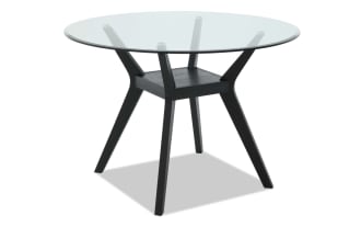 Modern round glass-top table with black wooden angled legs and a small rectangular shelf, ideal for contemporary dining or office spaces.