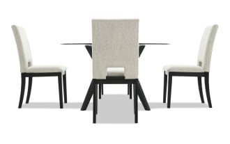 Modern dining set with four beige upholstered chairs featuring black wooden legs and a glass-top table with black angled legs, ideal for contemporary interiors.