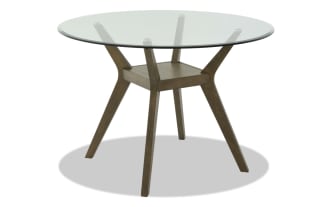 Round dining table with clear glass top and angled wooden legs in a natural brown finish, modern minimalist style.