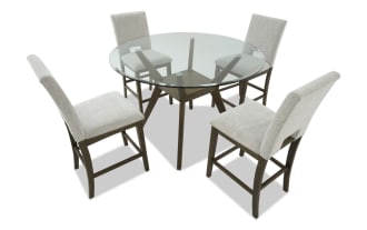 Round glass dining table set with four beige upholstered chairs featuring wooden legs and frames, modern farmhouse style.