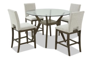 Round glass dining table set with four beige upholstered chairs featuring wooden legs and frames, modern farmhouse style.