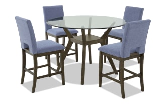 Round glass-top dining table with dark wood base and four blue upholstered chairs, featuring cushioned seats and wooden legs, suitable for modern dining rooms.